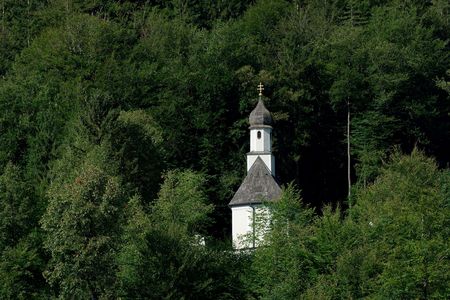 Weiße Kapelle mit Zwiebelturm, umgeben von dichtem Wald in kräftigem Grün